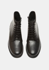 Bottines en cuir noir présentant une surface lisse, un bout rond et un laçage à l'avant avec un léger talon rehaussé.