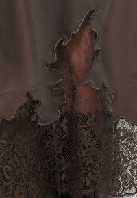 Brown layered fabric with lace trim at the hem. Features a leaf-shaped cutout, showcasing intricate floral lace patterns in a matching shade.