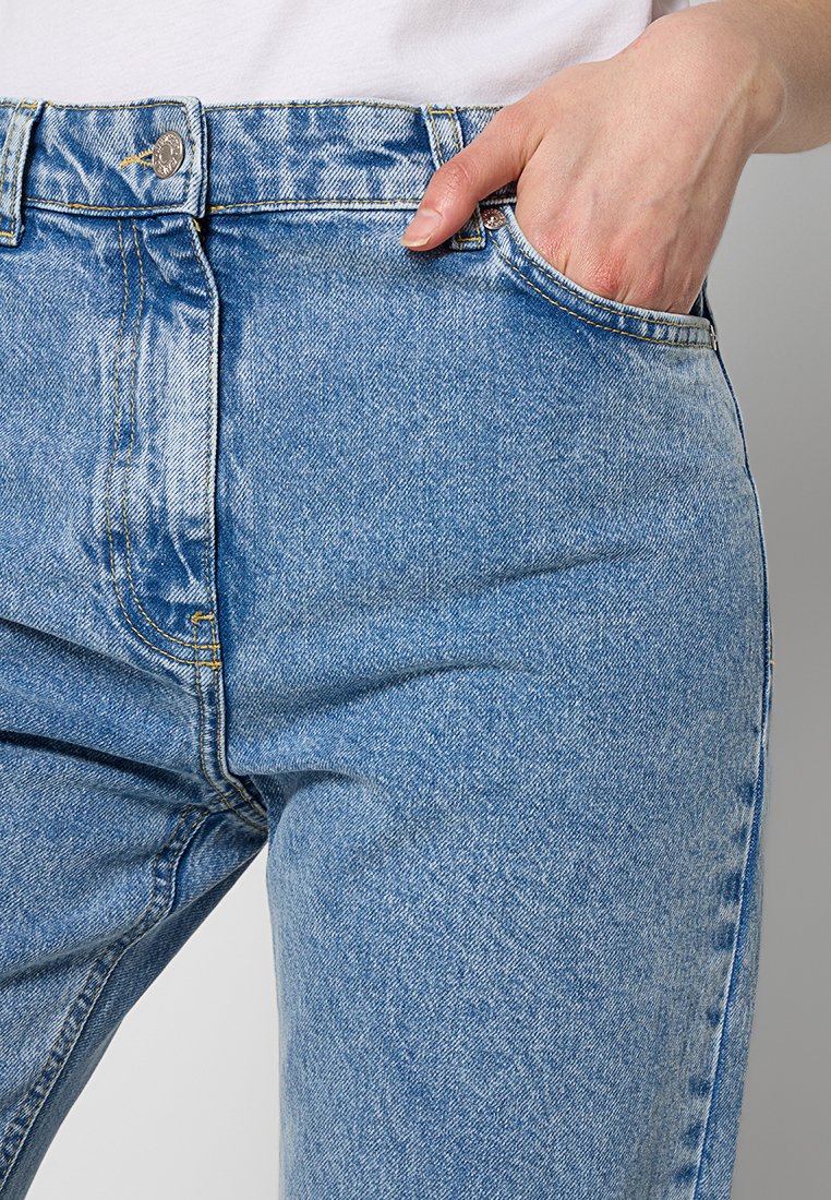 Jasnoniebieskie dżinsy z wysokim stanem, z kieszenią z przodu, żółtymi detalami przeszyć oraz zapięciem na guzik w talii.