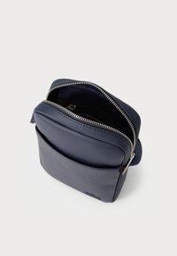 Geantă de culoare bleumarin, cu o suprafață texturată, sistem de închidere cu fermoar și o buzunar frontal. Design compact cu căptușeală netedă și accente din metal argintiu.