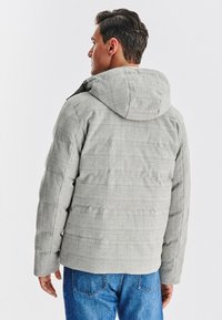 Szara pikowana kurtka puchowa w kratę z kapturem, z teksturą pikowania i luźnym krojem, zestawiona z niebieskimi dżinsami.