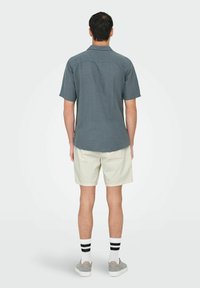 Camisa de botones gris de manga corta con una textura suave, combinada con pantalones cortos beige claro y calcetines a rayas en blanco y negro.