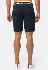 Marineblaue Shorts mit umgeschlagenen Säumen, ausgestattet mit einem gestreiften Bund, zwei Gesäßtaschen und sichtbarer Stoffstruktur im Materialdesign.