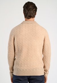 Beige stickad tröja med kabelmönster, ribbad nederkant och ärmslut samt klassisk krage. Mjuk textur med avslappnad passform.