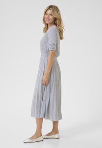 Gray, long-sleeved dress with a pleated skirt, featuring a fitted waist and ribbed texture. Paired with silver ballet flats.