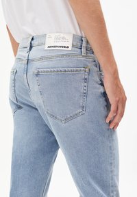 Jasnoniebieskie dżinsy z denimu o prostym kroju, z białą metką w pasie oraz dwoma tylnymi kieszeniami ozdobionymi przeszyciami.