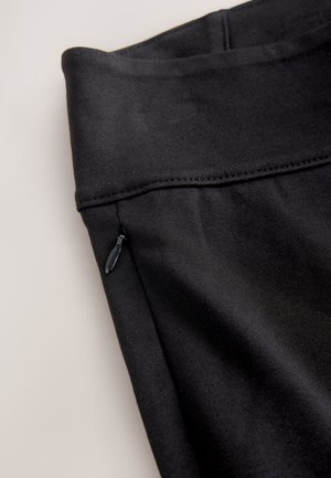 Juodos spalvos audinio leginsai su aukštu liemeniu, lygiu audiniu ir maža šonine kišenėle su užtrauktuku.