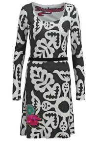 Robe à manches longues en noir et blanc avec des motifs floraux abstraits, ceinture noire fine, et détail coloré de fleurs roses et vertes près de l'ourlet.