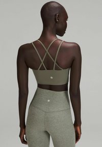 Sujetador deportivo verde oliva con tirantes entrecruzados y un logo en la parte posterior, combinado con leggings altos con textura que hacen juego.