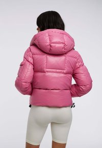 Rosa puffjacka med huva, med en blank yta, lätt vaddering och justerbar nederkant. Inkluderar sidofickor.
