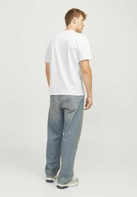 Camiseta de algodón blanca, de manga corta, corte relajado, combinada con pantalones vaqueros rectos de color azul claro y zapatillas grises. Diseño simple sin patrones.