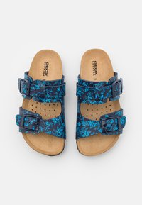 Sandalias de dedo con dos hebillas ajustables azules, con una base azul marino decorada con un brillo azul de patrón abstracto y una plantilla de corcho.