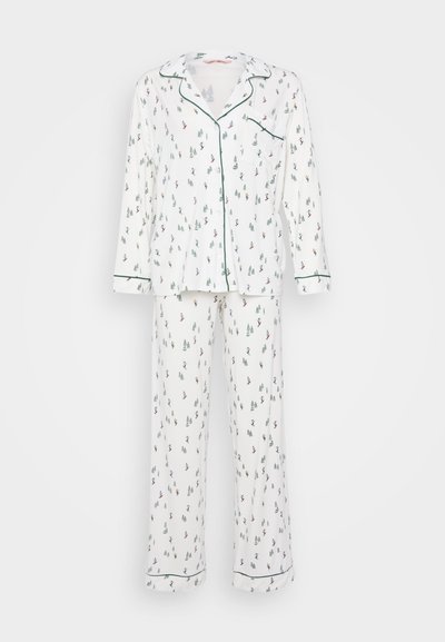 Άσπρο σετ πιτζάμας με εκτυπωμένο σχέδιο δέντρων και σκιέρ, με σκούρο πράσινο ρέλι γύρω από το γιακά και τις μανσέτες. Μακρυμάνικη μπλούζα και παντελόνι.