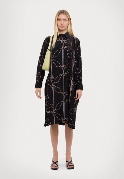 Čierne šaty s farebnými vzormi listov, dlhými rukávmi a zapínaním na gombíky. Kombinované s svetlozelenou kabelkou a čiernymi sandálmi na remienky.
