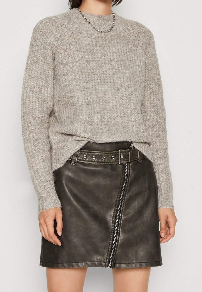 Jasnoszara, prążkowana wełniana bluzka połączona z czarną skórzaną spódnicą z zamkiem z przodu i ćwiekowanym paskiem. Casualowy i teksturowany wygląd.