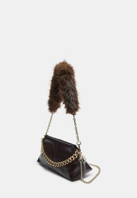Sac à main en cuir marron avec une poignée en fausse fourrure, des accents en chaîne dorée et une forme structurée. Présente une finition brillante profonde et des coutures robustes.