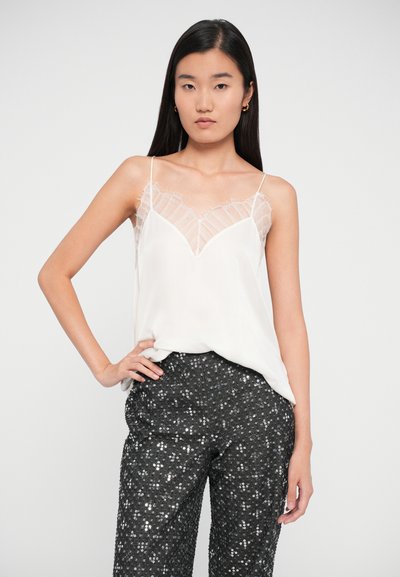 Hvit cami topp med gjennomsiktig blonde detalj langs en dyp V-hals, kombinert med svarte paljettbukser. Glatt stoff med justerbare stropper.