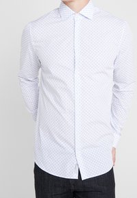 Vit skjorta med knappar och en diskret blå bladmönster, långa ärmar, klassisk krage och slät bomullstyg.