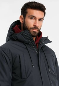 Dunkelblaue Daunenjacke mit hohem Kragen, Reißverschluss und verstellbaren Kordeln. Verfügt über eine Brusttasche und eine weiche, glatte Textur.