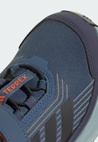 Kék sportcipő, hálós felsőrésszel, gumitalppal és szürke részletekkel. Jellemzője a struktúrált felület és az elasztikus fűzőrendszer, melyen a "TERREX" logó található.