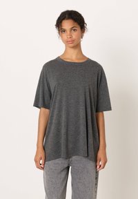 Siv kratka majica z okroglim izrezom iz mehkega blaga; ohlapen kroj s ravnim robom. Nošena z svetlo sivimi teksturiranimi jeans hlačami.