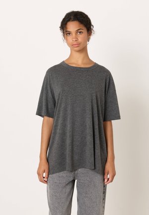 Pilkas trumpomis rankovėmis marškinėlis su apvalia apykakle, pagamintas iš minkštos medžiagos; laisvo kirpimo su tiesia apačia. Dėvimas su šviesiai pilkais struktūruotais džinsais.