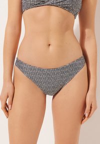 Svart och vit mönstrad bikiniunderdel med låg midja, slät textur och minimalistisk design, lämplig för badkläder.