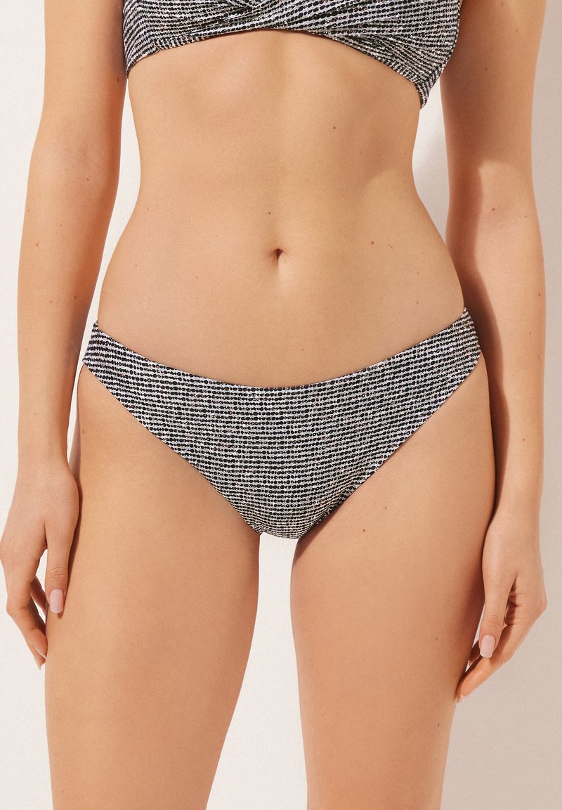 Svart och vit mönstrad bikiniunderdel med låg midja, slät textur och minimalistisk design, lämplig för badkläder.