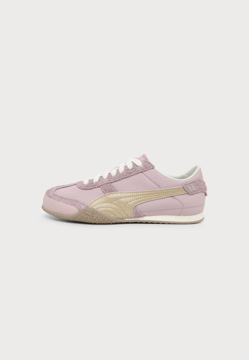 Une basket basse rose et beige avec des lacets blancs et une semelle texturée présentée sur un fond gris clair uni.