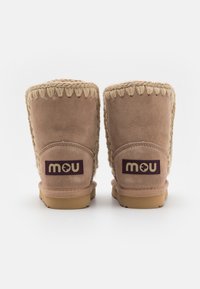 Bottines en suede beige avec une épaisse semelle en caoutchouc beige, des coutures le long du bord supérieur et un patch de marque au talon.