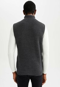Gilet in maglia a coste grigio con colletto alto, forma aderente e maniche lunghe bianche a contrasto. La texture morbida è evidente.