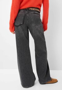 Schwarzweilige Jeans mit weitem Bein aus Denim im verblassten Finish, Rückentaschen und einem Leopardenmuster-Gürtel. Getragen mit braunen Wildleder Slippern.