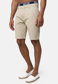 Shorts beige con un patrón y una cinturilla azul marino que presenta "INDICODE". Fabricados con un tejido texturizado; de largo hasta la rodilla y con bolsillos frontales.