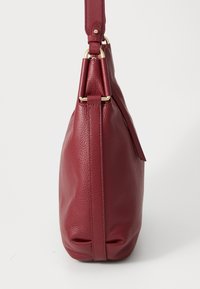 Sac à main en cuir rouge avec une finition texturée, dotée d'un fond plat, d'une bandoulière réglable et de détails en métal doré sur les côtés.