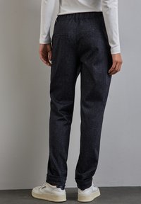 Mörkblå texturerade byxor med slim fit, försedda med elastiskt midjeband och uppvikt fåll, i kombination med vita sneakers.