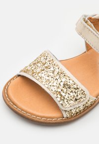 Sandales dorées scintillantes avec deux larges brides, semelle intérieure en cuir bronzé et bord cousu. Dessus texturé orné de sequins étincelants.