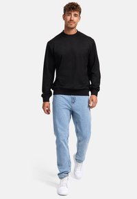Sudadera de forro polar negra con cuello redondo, combinada con jeans de denim azul claro y zapatillas blancas, con un corte relajado y puños acanalados.