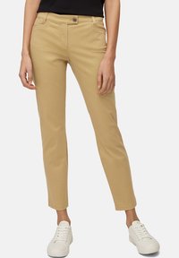 Chinos beiges à coupe slim, dotés d'une fermeture à boutons, de poches avant et d'une texture lisse, associés à des baskets blanches.