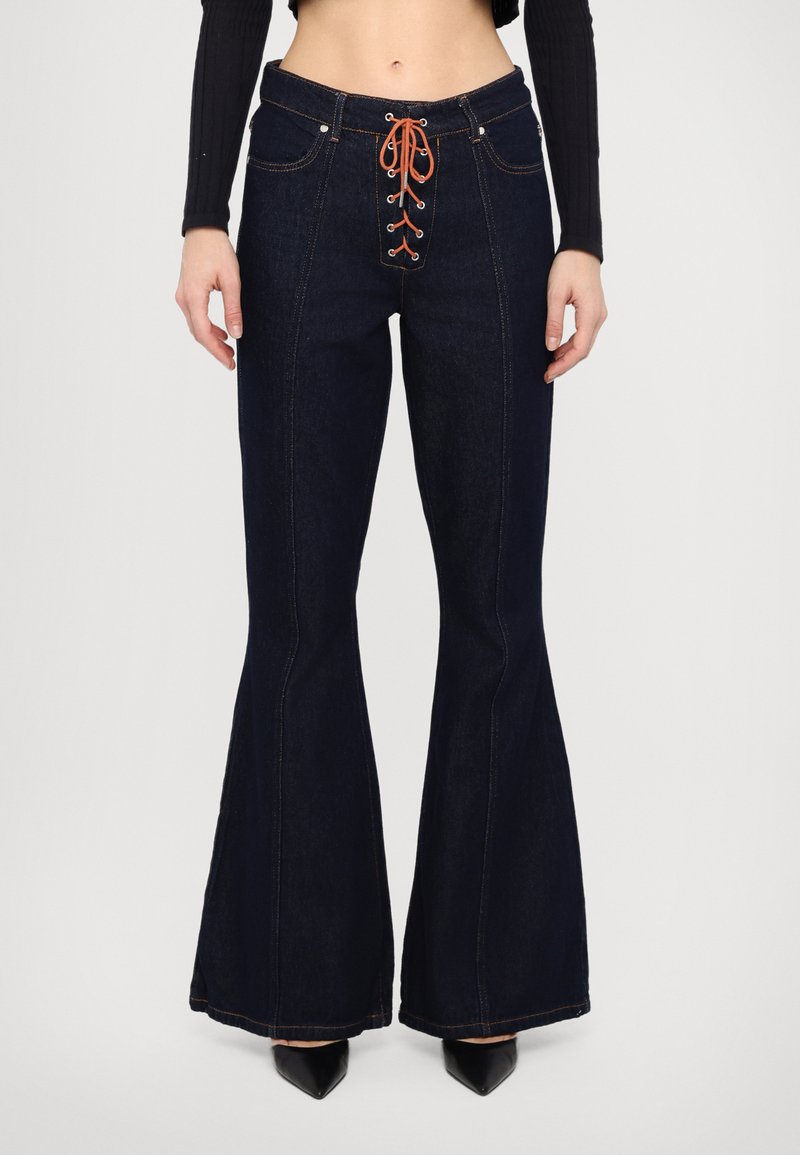 Vaqueros de mezclilla azul oscuro acampanados con cintura alta, que presentan un frontal con cordones naranjas, costuras contrastantes y un diseño clásico de cinco bolsillos.