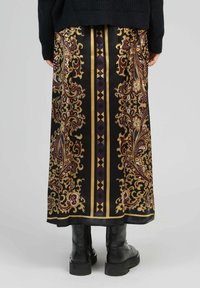 Jupe noire avec des motifs paisley dorés et bordeaux complexes, ornée de rayures verticales et d'accents géométriques, fabriquée en tissu lisse.