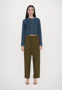 Blå kabelstickad cardigan med rund halsringning och framknappning, matchad med olivgröna cargobyxor med fickdetaljer.