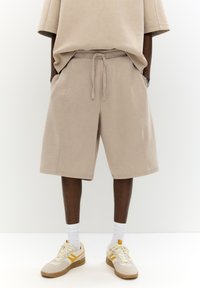 Pantaloni scurți din bumbac bej cu un tiv elastic, buzunare laterale și o croială confortabilă. Asortați cu adidași bej cu accente galbene.