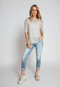 Beige Kurzarmoberteil, kombiniert mit hellblauen hochgekrempelten Jeans und beigen Sneakers. Das Oberteil hat eine lockere Passform und eine weiche Textur.