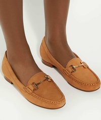 Tan suède instappers met een lage houten hak, voorzien van een gouden kettingaccent over de wreef en contrasterende stiksels rond de randen.