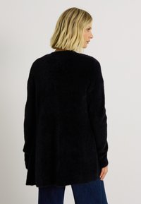 Cardigan noir en tricot duveteux à coupe décontractée, manches longues et ourlet arrondi. Texture douce et design minimaliste.