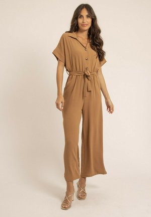 Combinaison marron à manches courtes, avec des boutons sur le devant et une taille cintrée. Fabriquée en tissu doux, elle présente une coupe ample et un design à jambes larges.