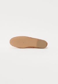 Suola di scarpa piatta marrone con texture intrecciata ai bordi, centro beige liscio e un sottile motivo di presa. Design leggero e flessibile.