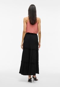 Jupe maxi noire à volants, avec des bordures en dentelle, associée à un débardeur rose texturé à fines bretelles. Tissu lisse et fluide.