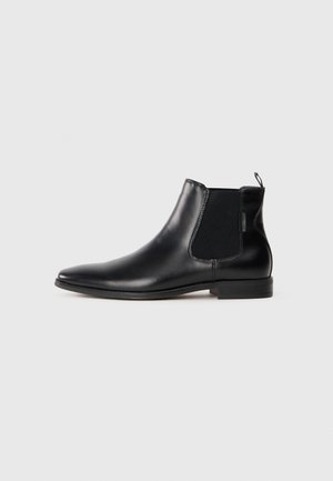 Bota de tobillo de cuero negro con un acabado suave, paneles laterales elásticos y un lazo de tirón; cuenta con una puntera redondeada y un tacón plano.
