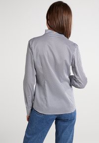 Svart och vitmönstrad långärmad skjorta med hög krage, splittrad bak, texturerad tyg och figurnära design med rundad nederkant.